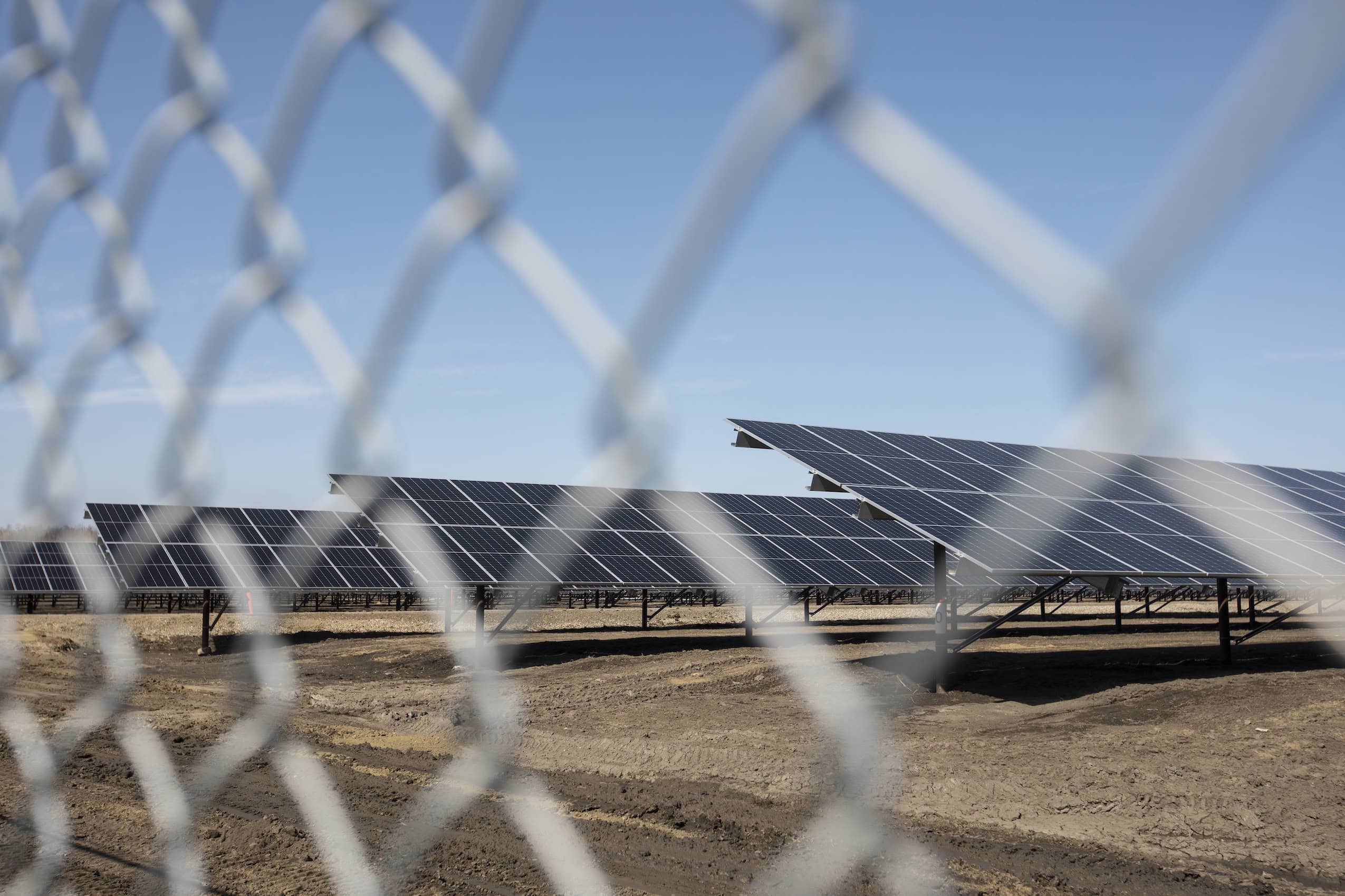 An array of solar panels is seen through a chain link fence.