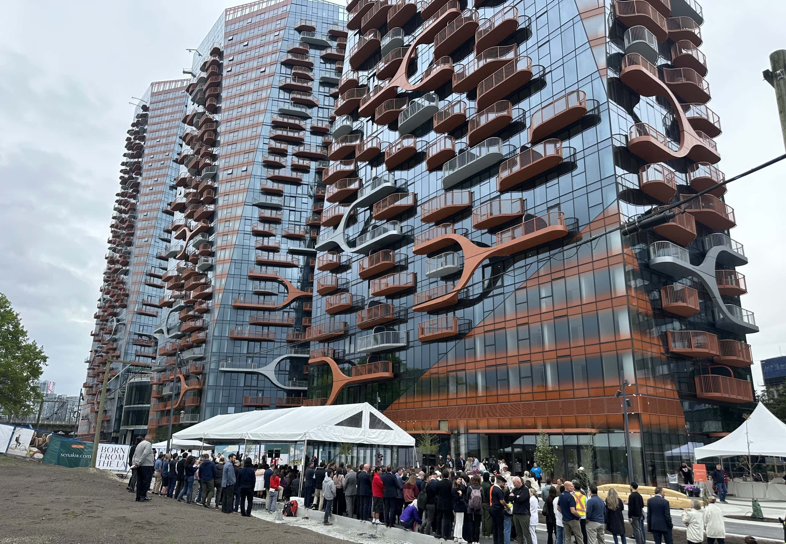 People gather at the base of two residential towers, called Sen̓áḵw.