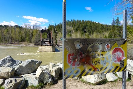 The Kettle Valley Rail bridge broken off from the rest of the trail, with water flowing beneath it. A sign in front reads "trail closed."