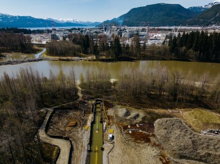 Industrial development alongside a river emptying into a bay with mountains in background