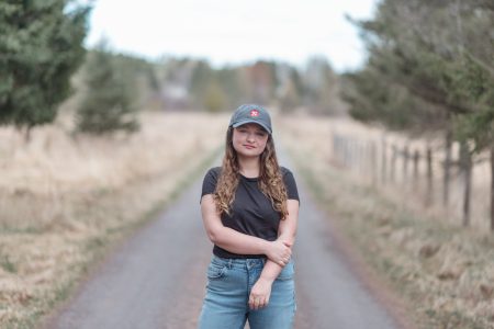 Journalist Leah Borts-Kuperman stands on a pathway and looks at the camera. She is wearing a hat with The Narwhal's logo on it.