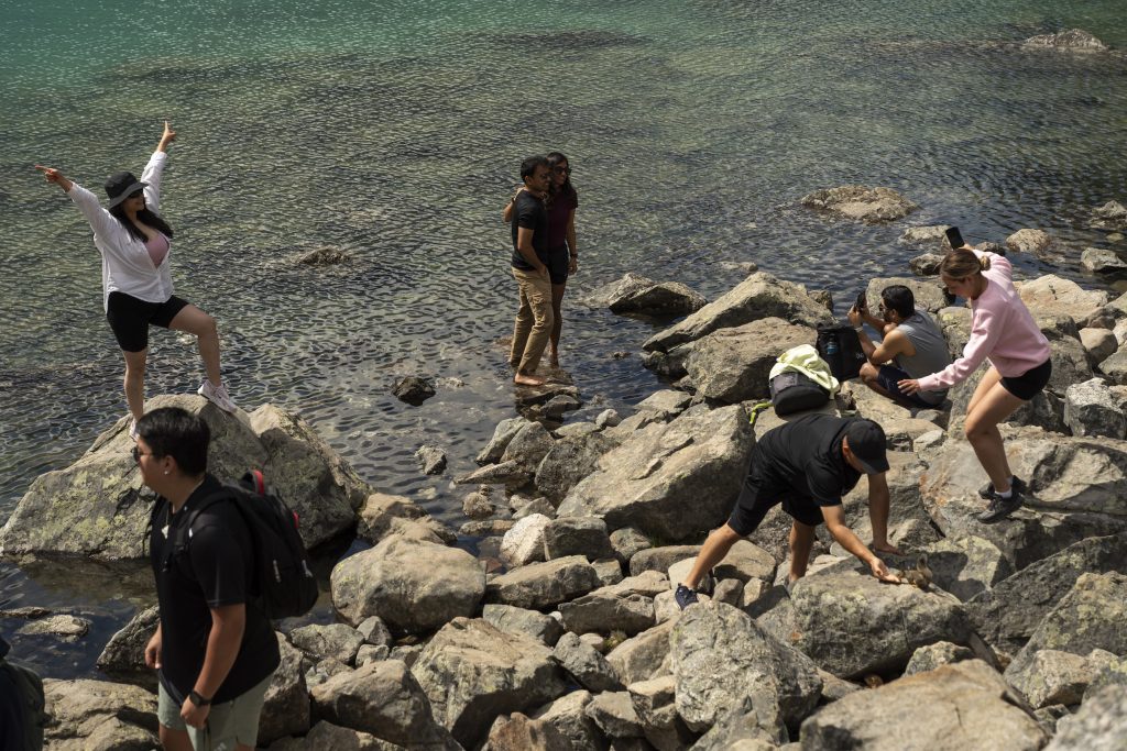 Visitors scramble on a rocky shore and pose for photos at Joffre Lakes Park in British Columbia.