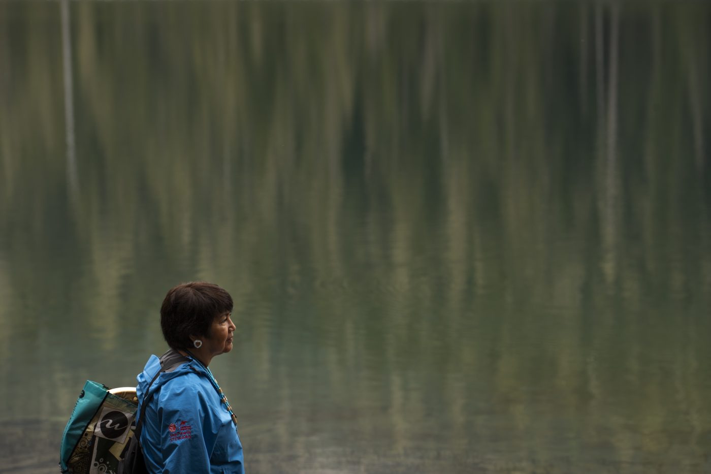 A person stands at the edge of a still lake that is reflecting images of trees.