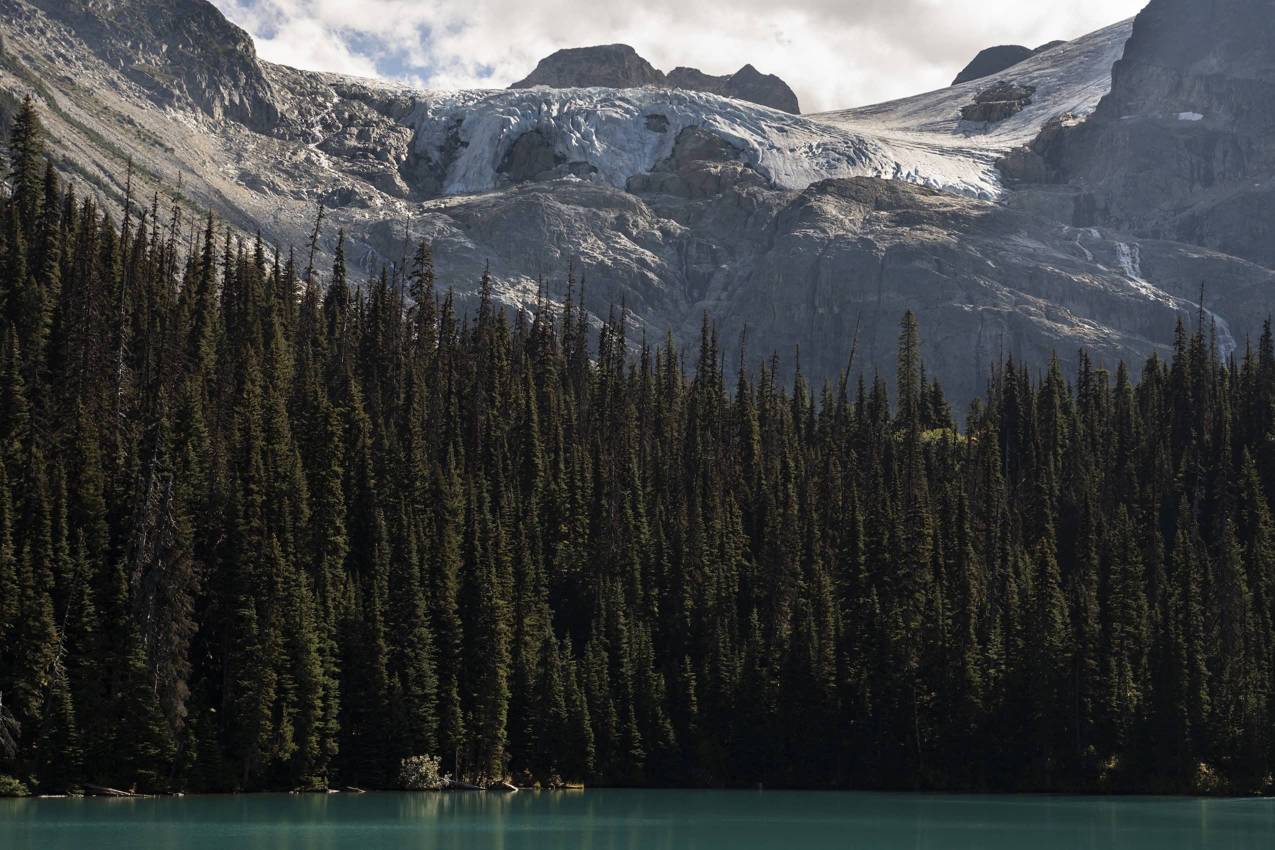 Mountains and coniferous trees rise above a still, emerald green lake at Joffre Lakes Park in British Columbia.