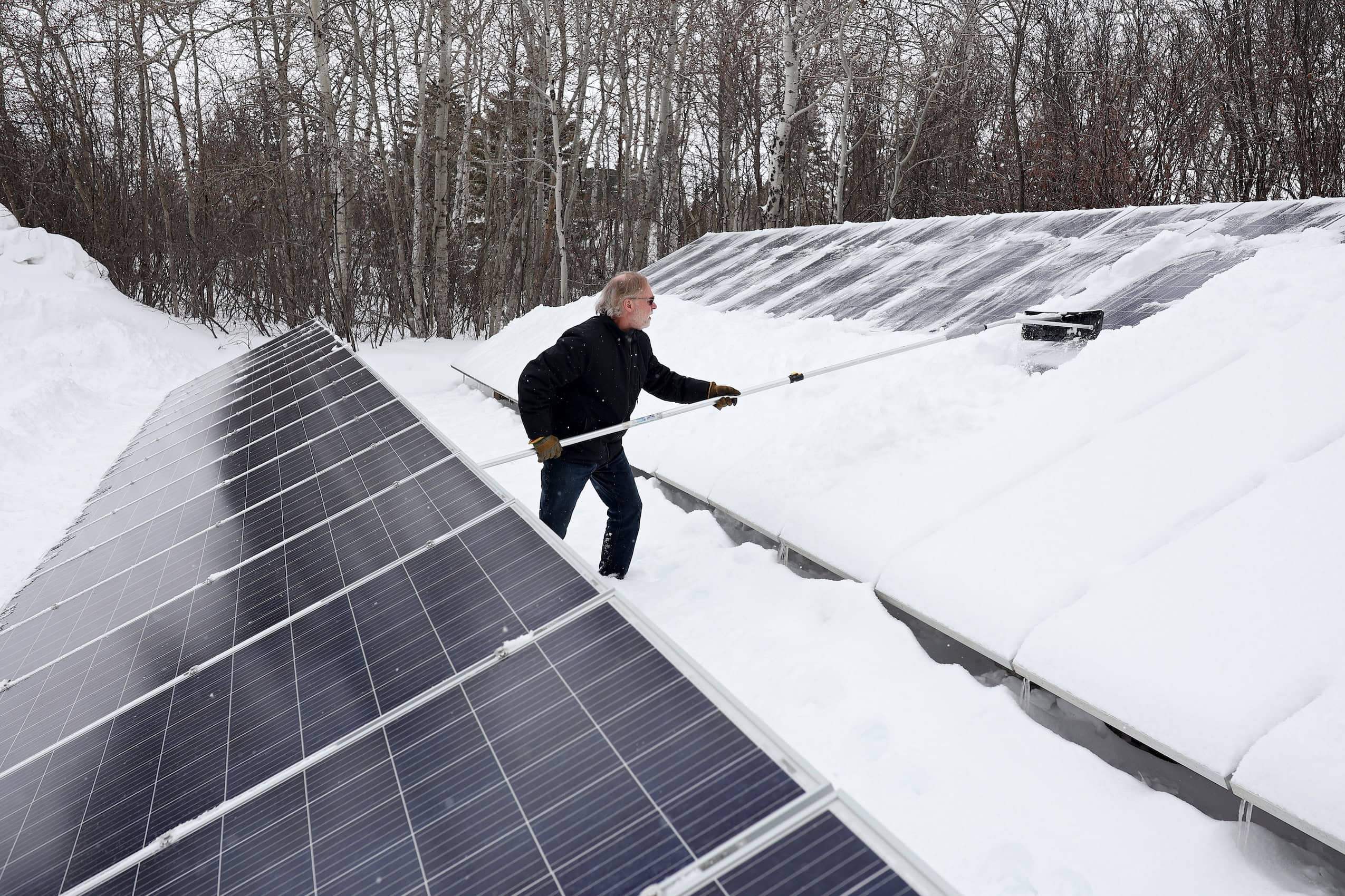 A man shovels snow off of solar panels.