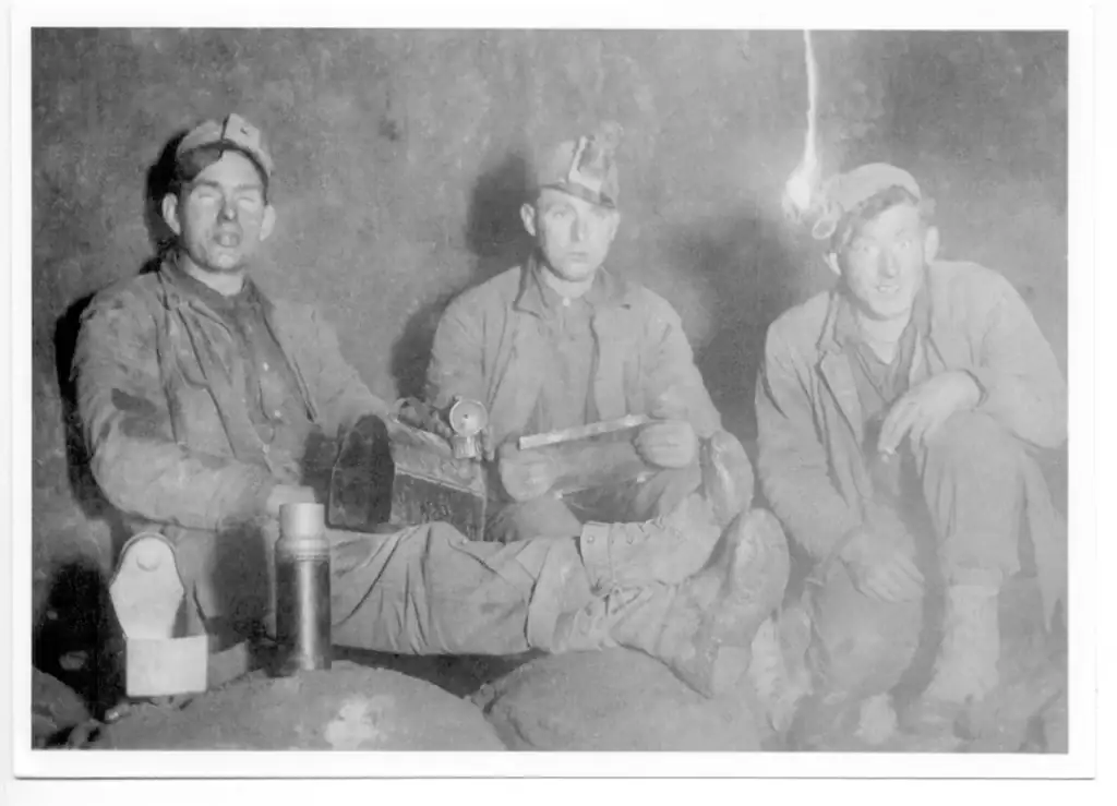 A black and white archival image from around 1923 of three miners underground with lunch boxes.