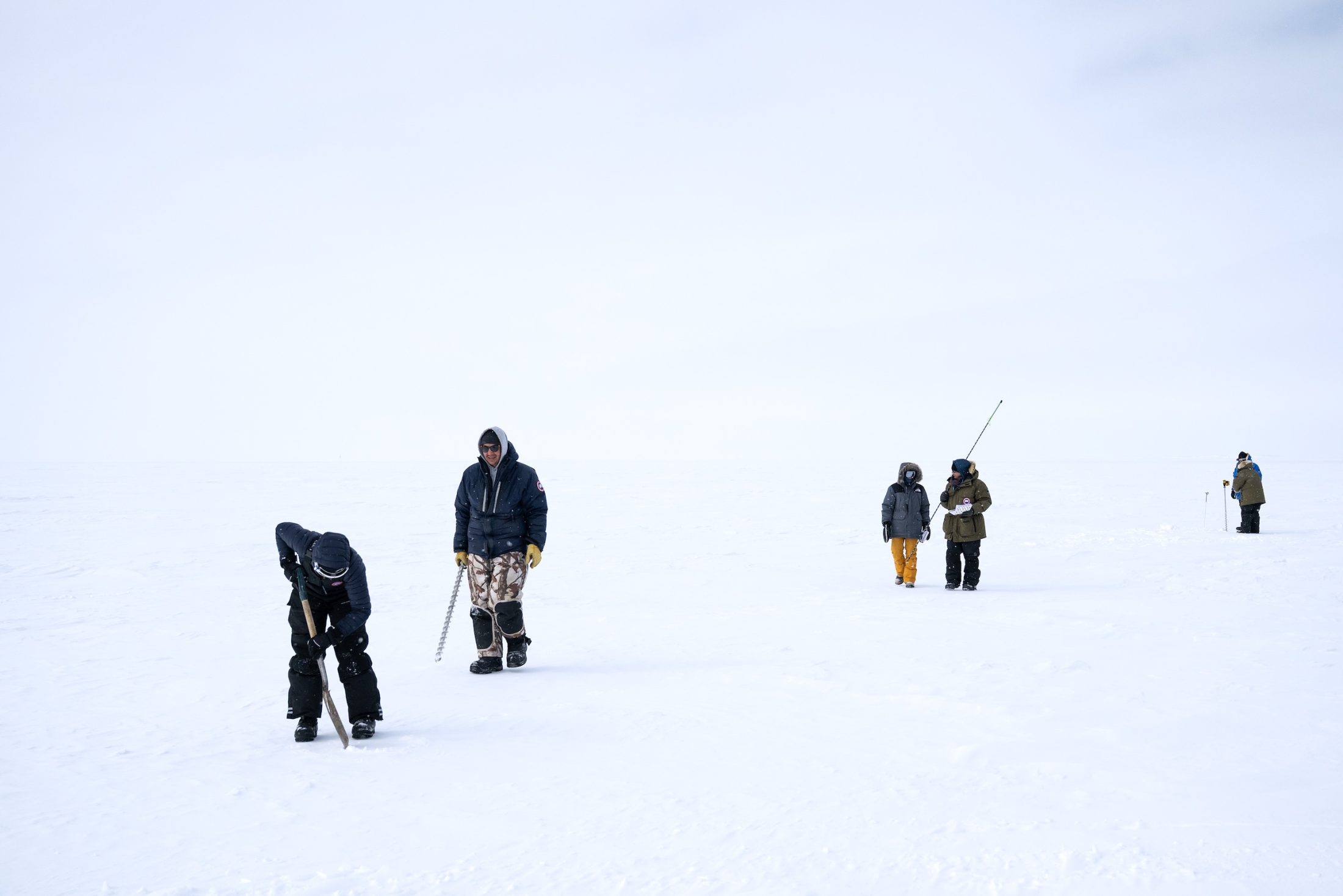 Six people in winter gear walk on sea ice.