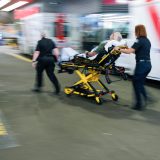 Two paramedics wheel a patient in a stretcher toward the entrance of the emergency department at the Vancouver General Hospital.