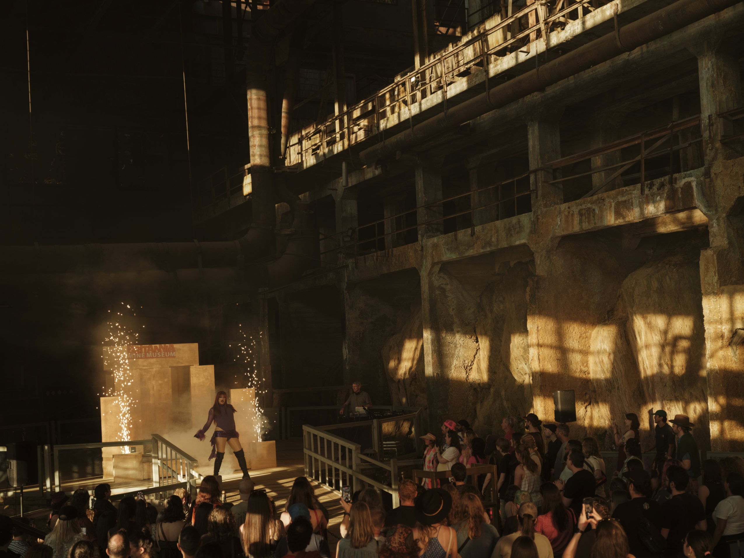 A drag artist performs for a crowd in a former copper mine, with fireworks going off behind them.
