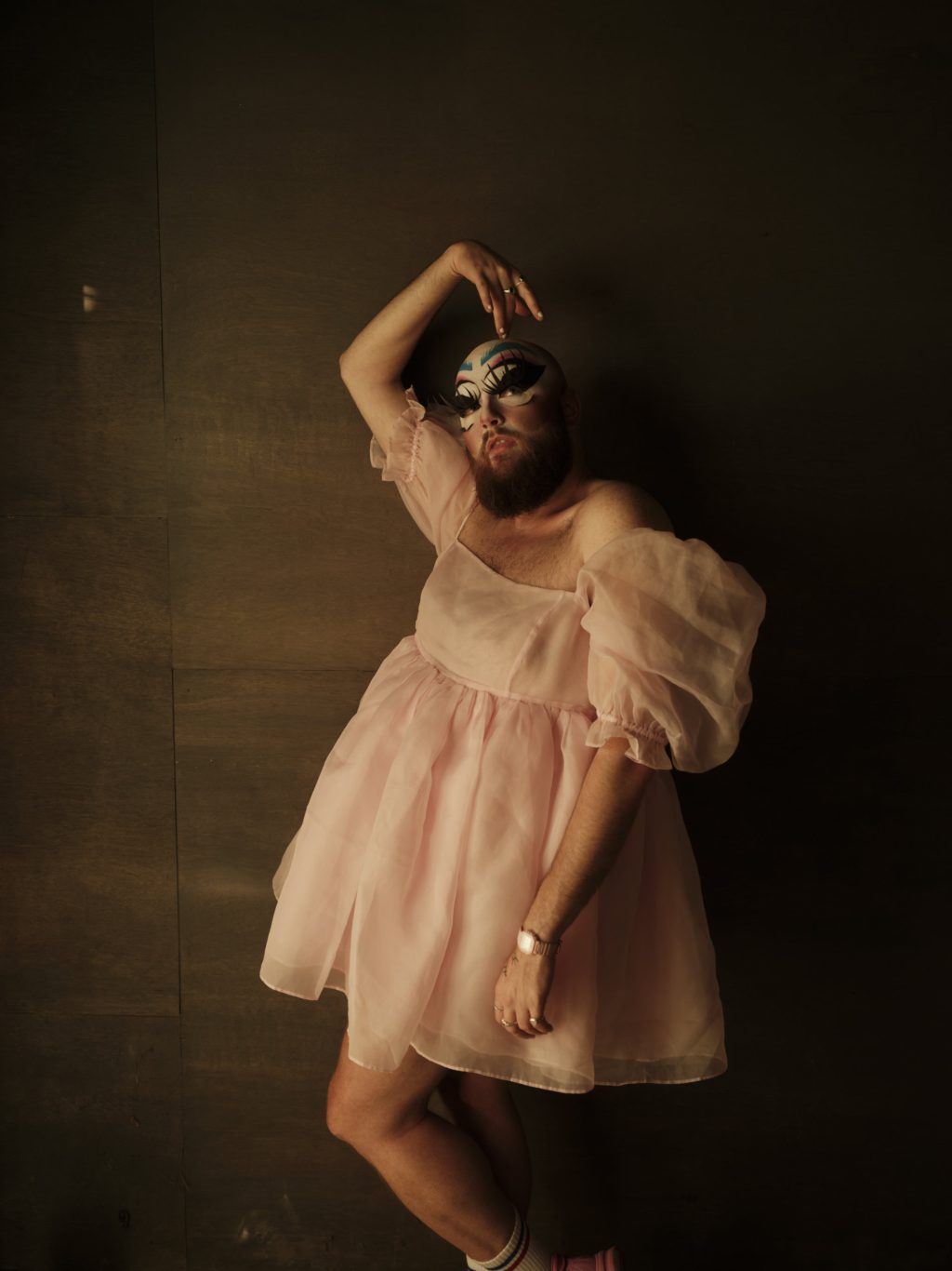 Drag artist Dust Cwaine, wearing a pink dress and face makeup, poses for a photo.