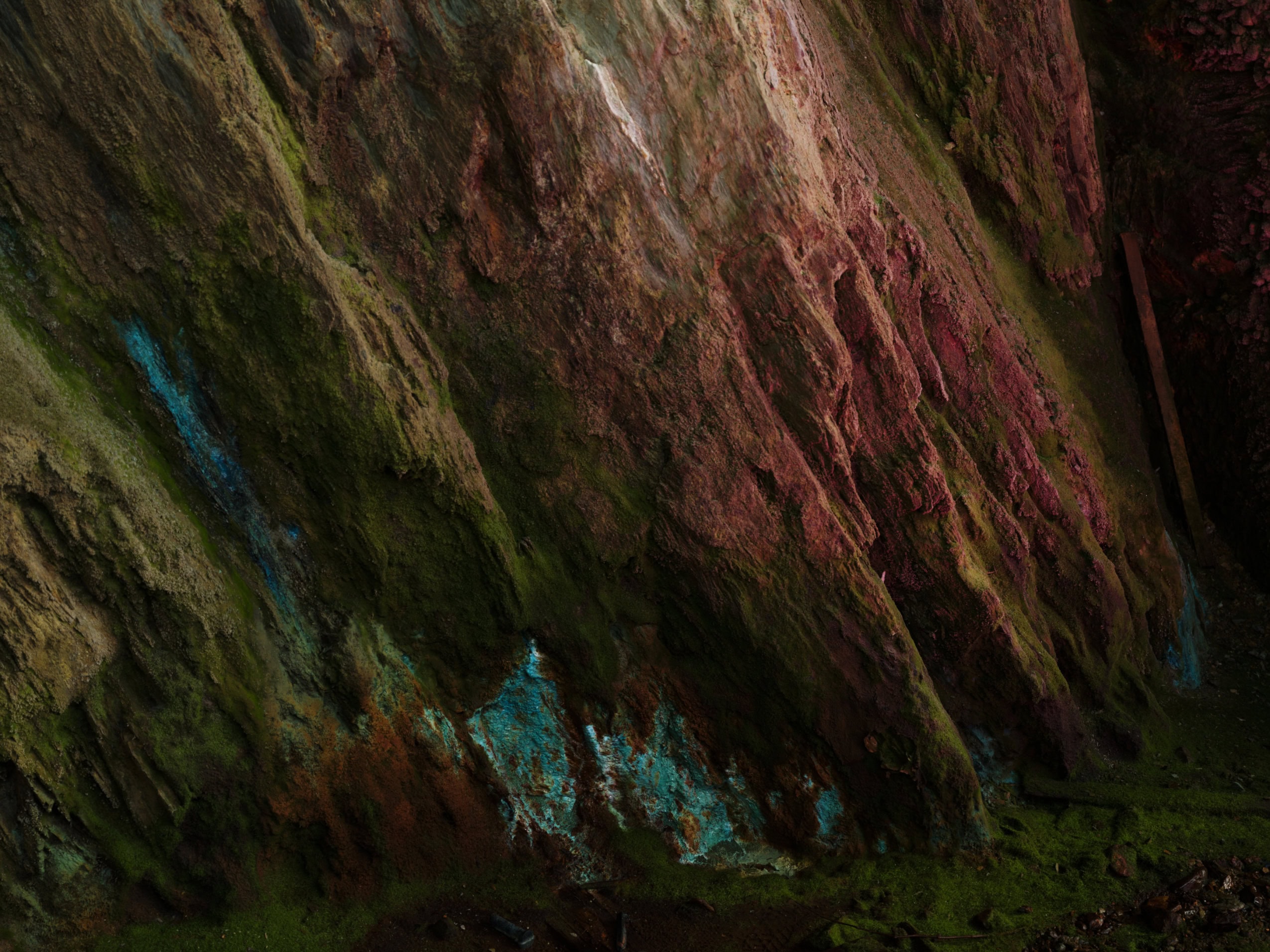 Unrefined copper deposits gleam turquoise on a rock wall.