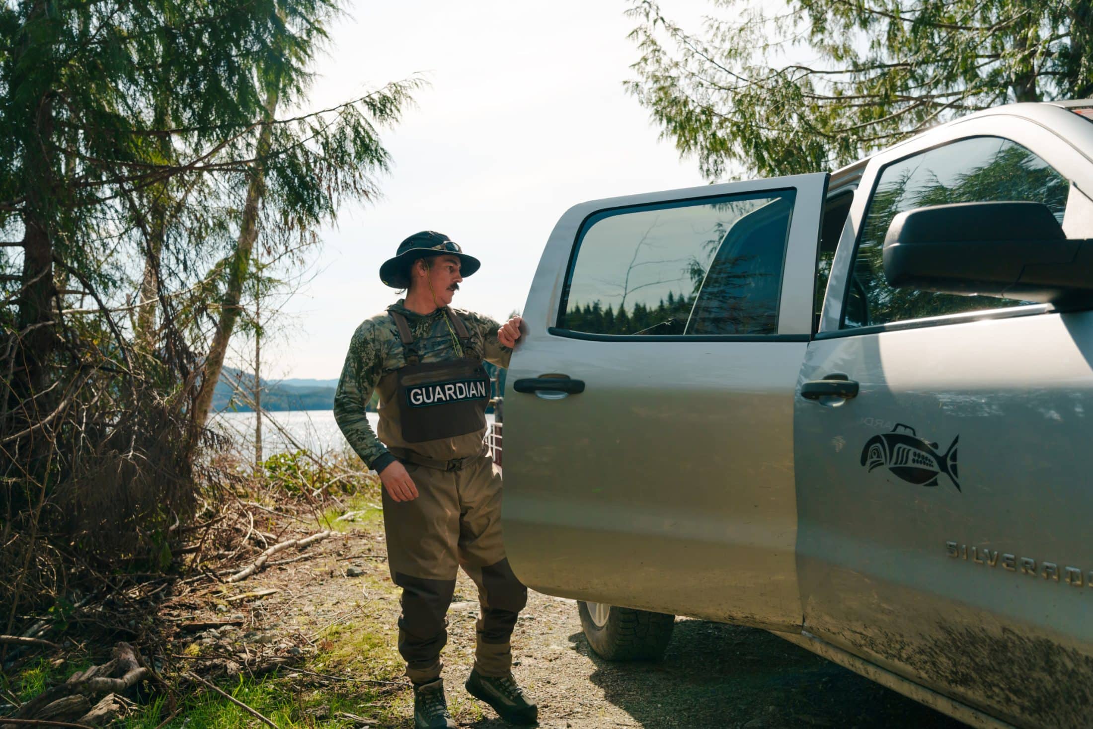 An Indigenous land guardian opens the back door of a pickup truck parked in a wilderness area.