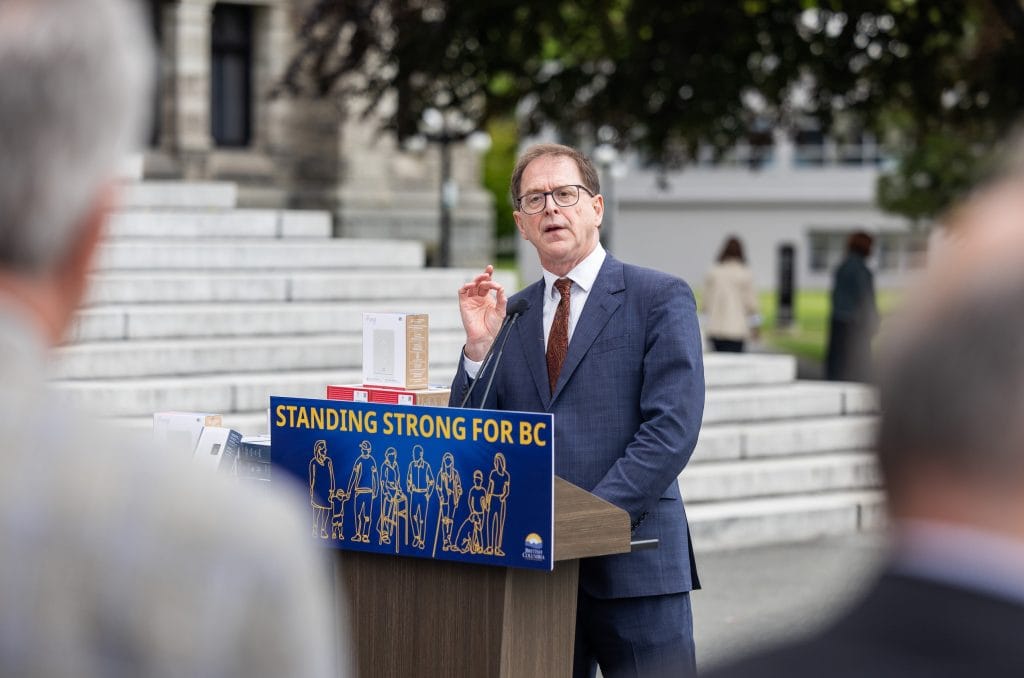 B.C. Minister of Energy and Climate Solutions Adrian Dix speaks at a lectern, in front of a sign that reads, "Standing strong for BC."