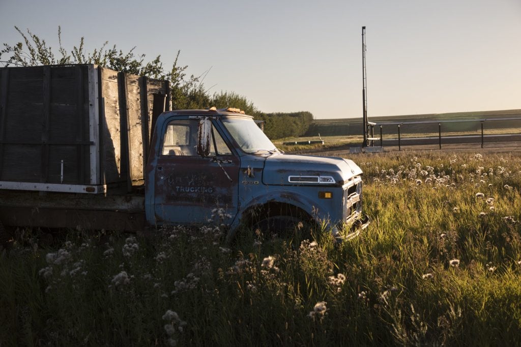 An old truck sits in a field, bathed in golden twilight.
