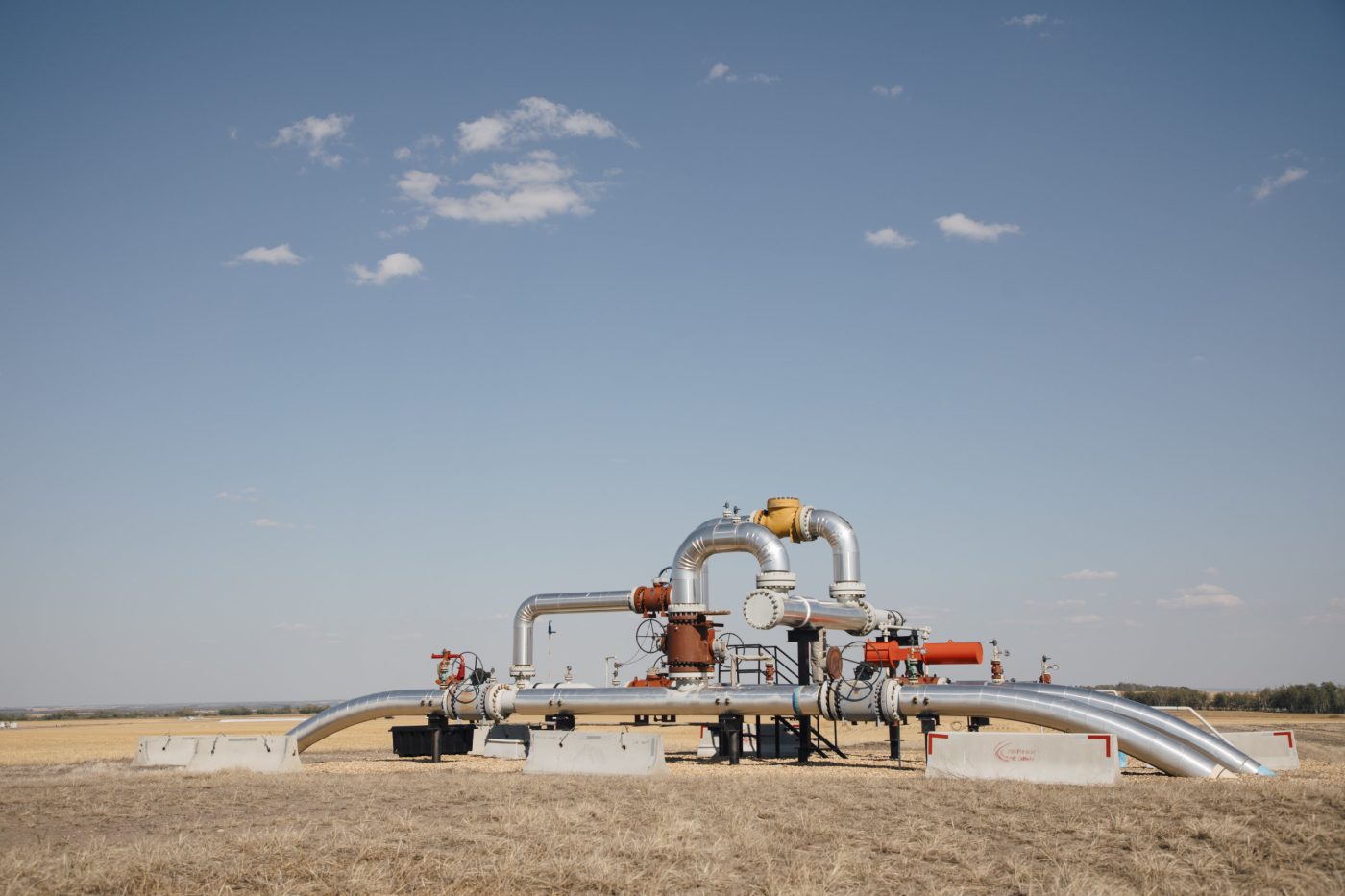 Oil and gas infrastructure in a rural field under a blue, mostly cloudless, sky in Dawson Creek, B.C.