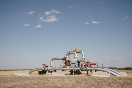Oil and gas infrastructure in a rural field under a blue, mostly cloudless, sky in Dawson Creek, B.C.