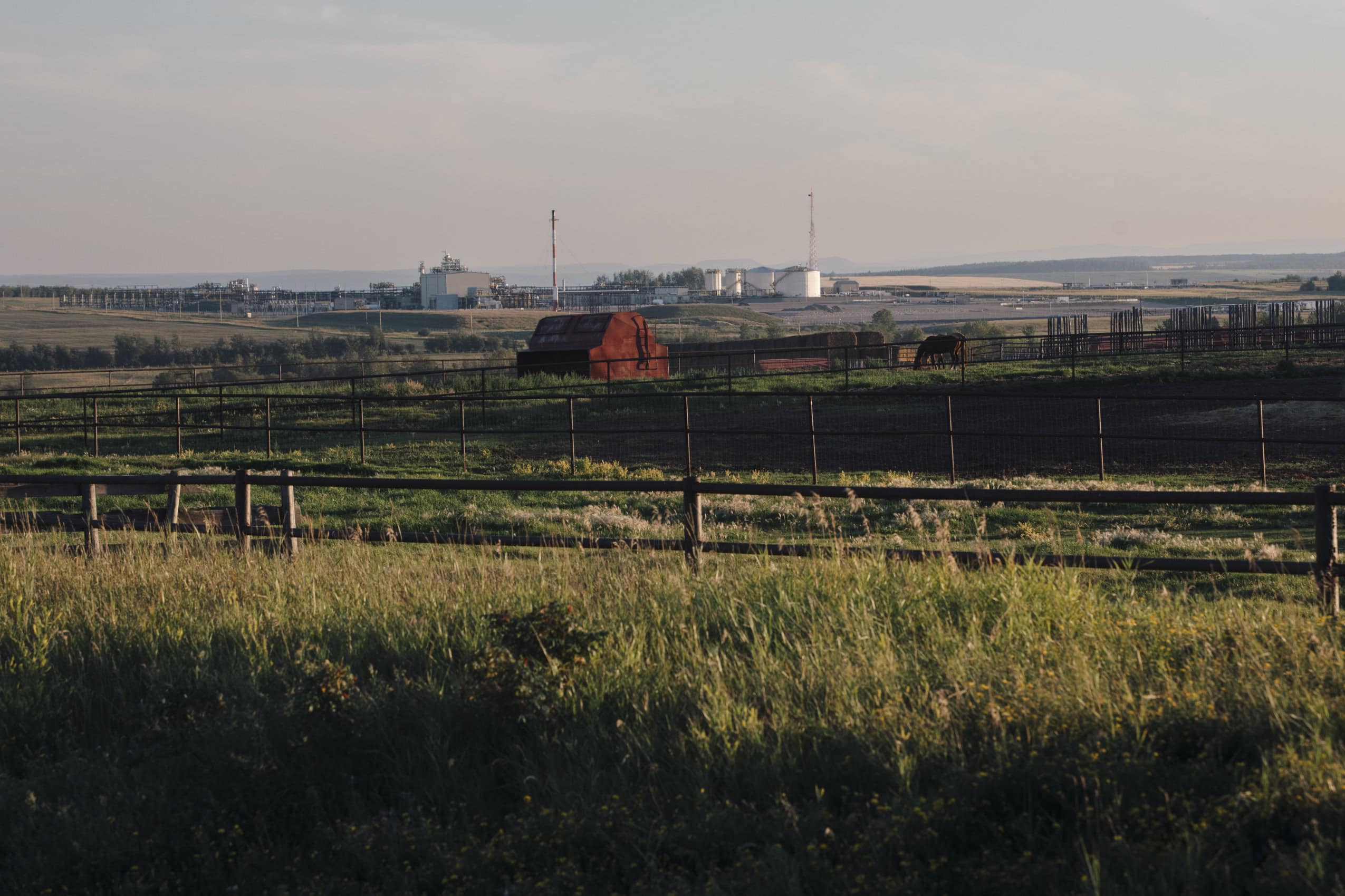 Rural fields at twilight. In the distance, a natural gas plant.