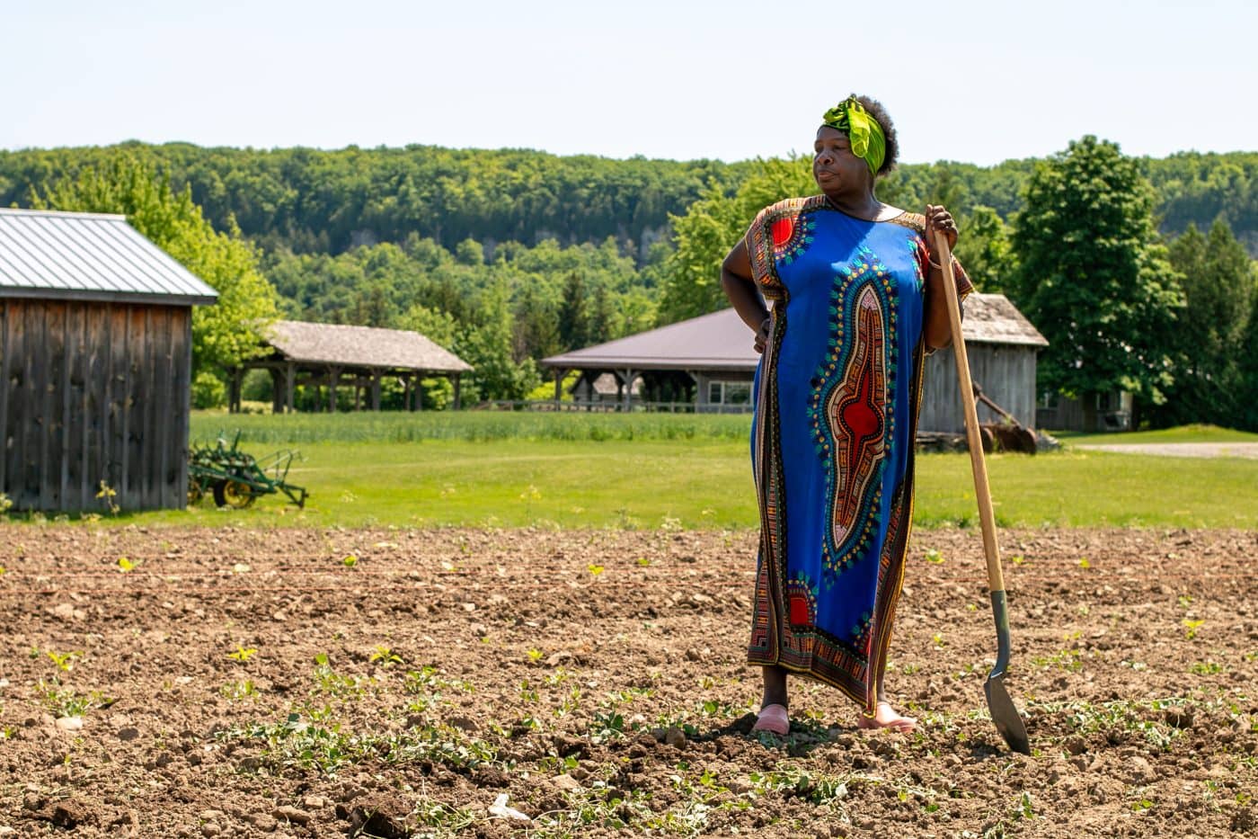 A woman in bright coloured clothing holds a shovel, standing on a farm