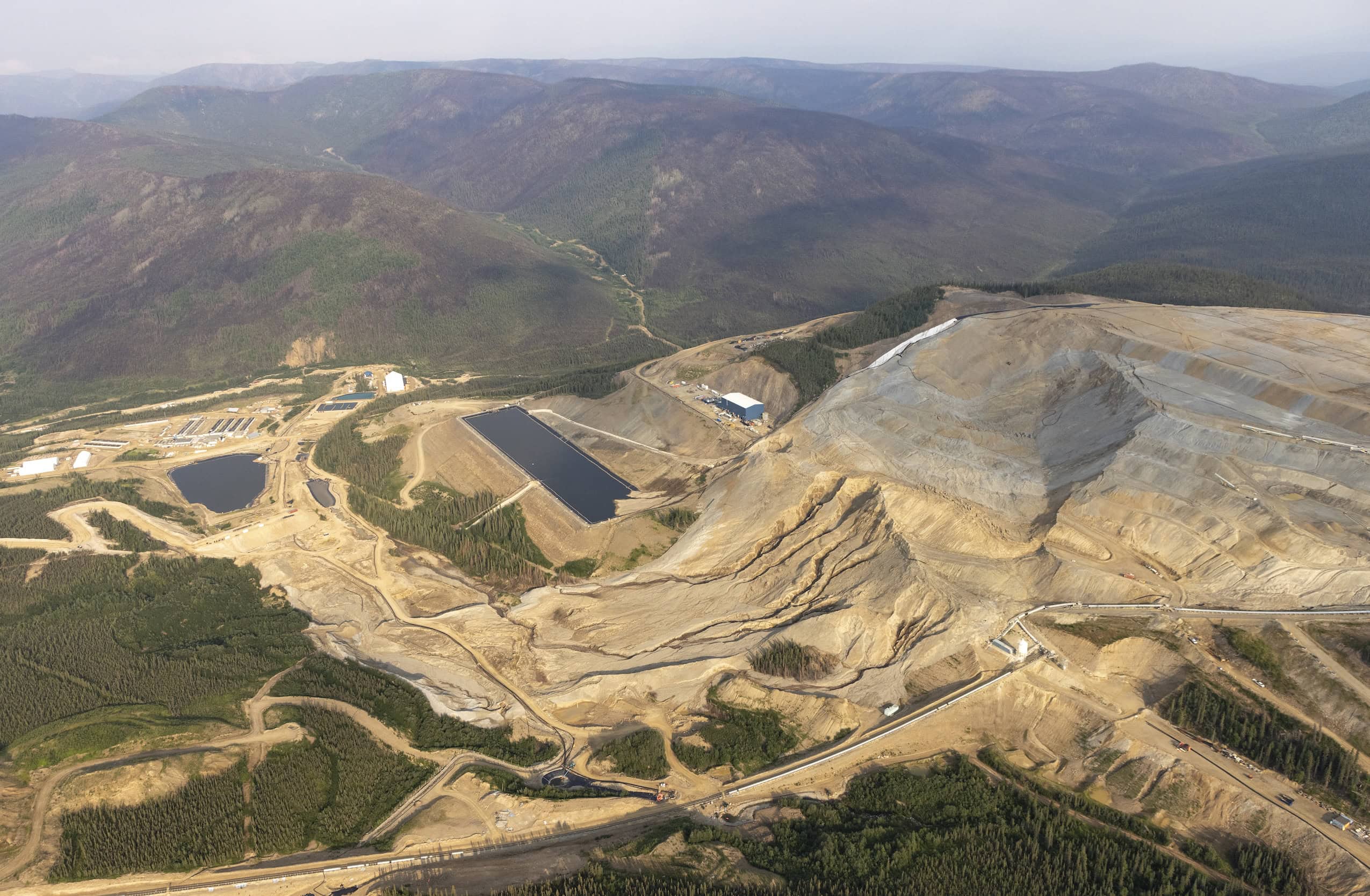 Aerial view of an open-pit mine with brown, barren hills and a tailings pond.