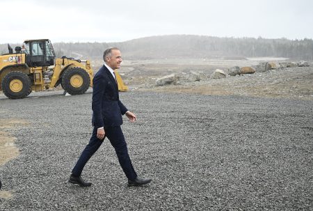 Canadian Prime Minister Mark Carney walks through a light rain at an industrial site.