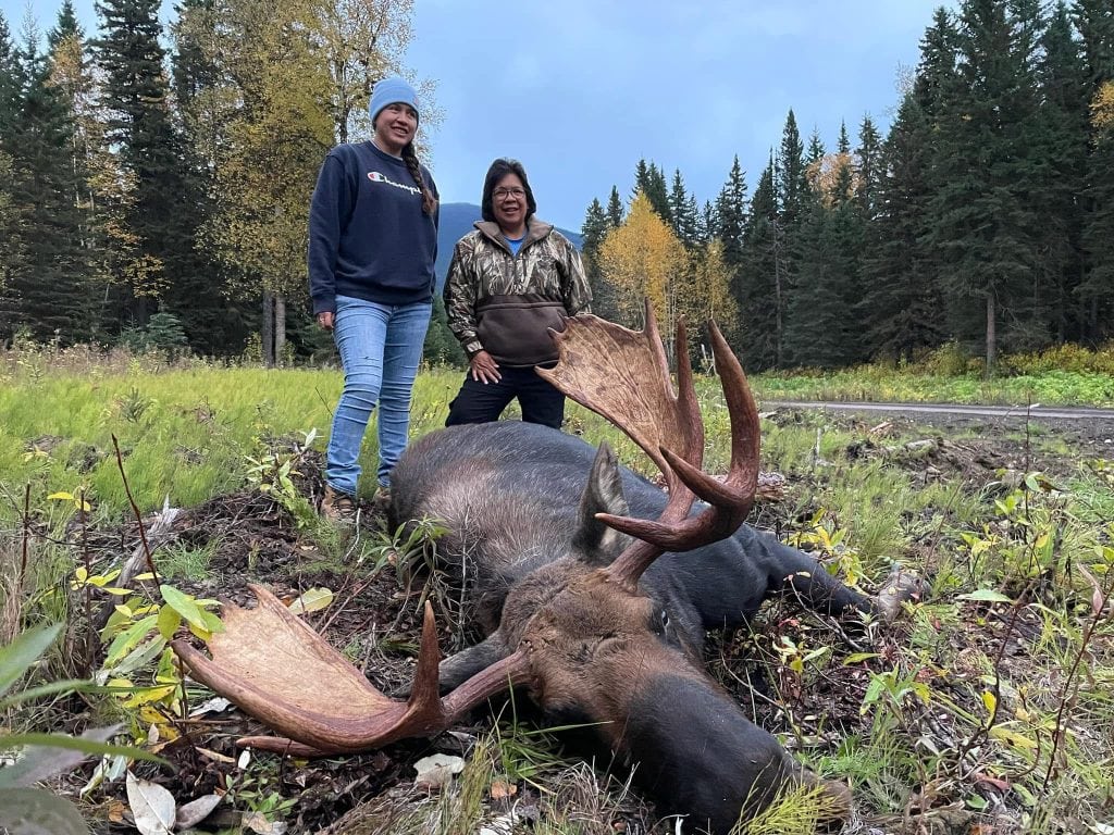 Two women are pictured behind a moose that has been shot in a hunt.