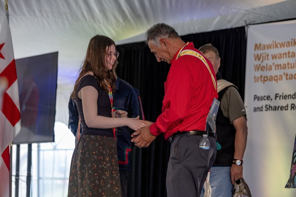 Two people shake hands on a stage.