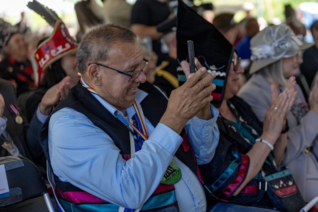 A man sitting in an audience takes a photo with his phone.