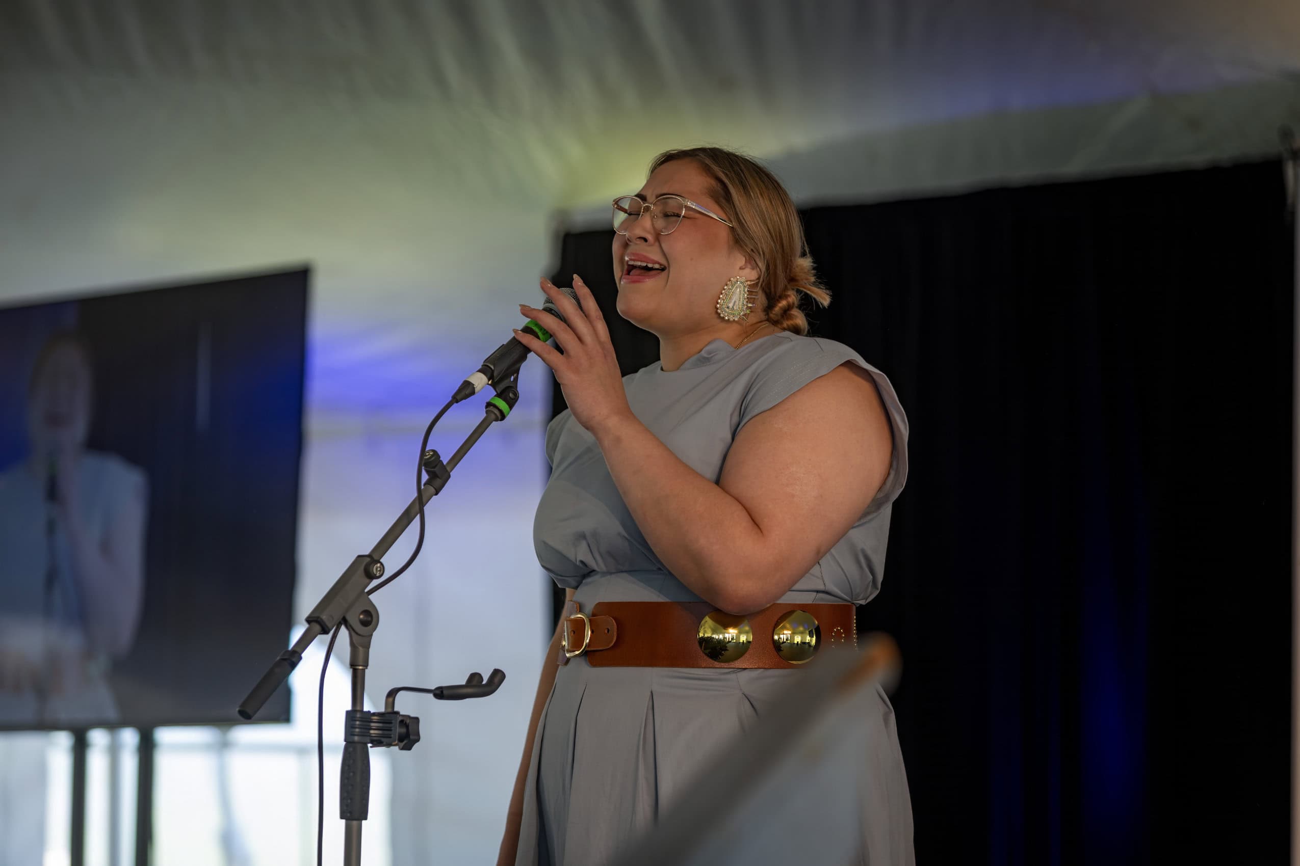 A woman in a grey dress sings into a microphone.