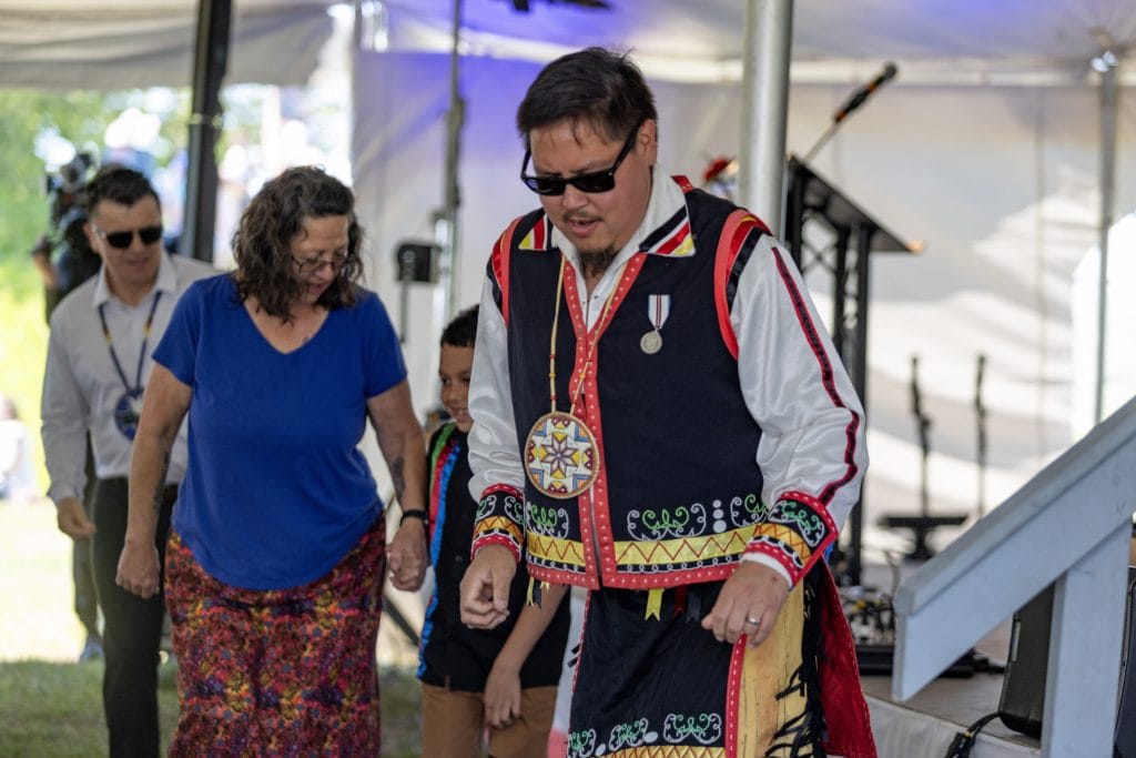 A man wearing Indigenous regalia dances on a stage.