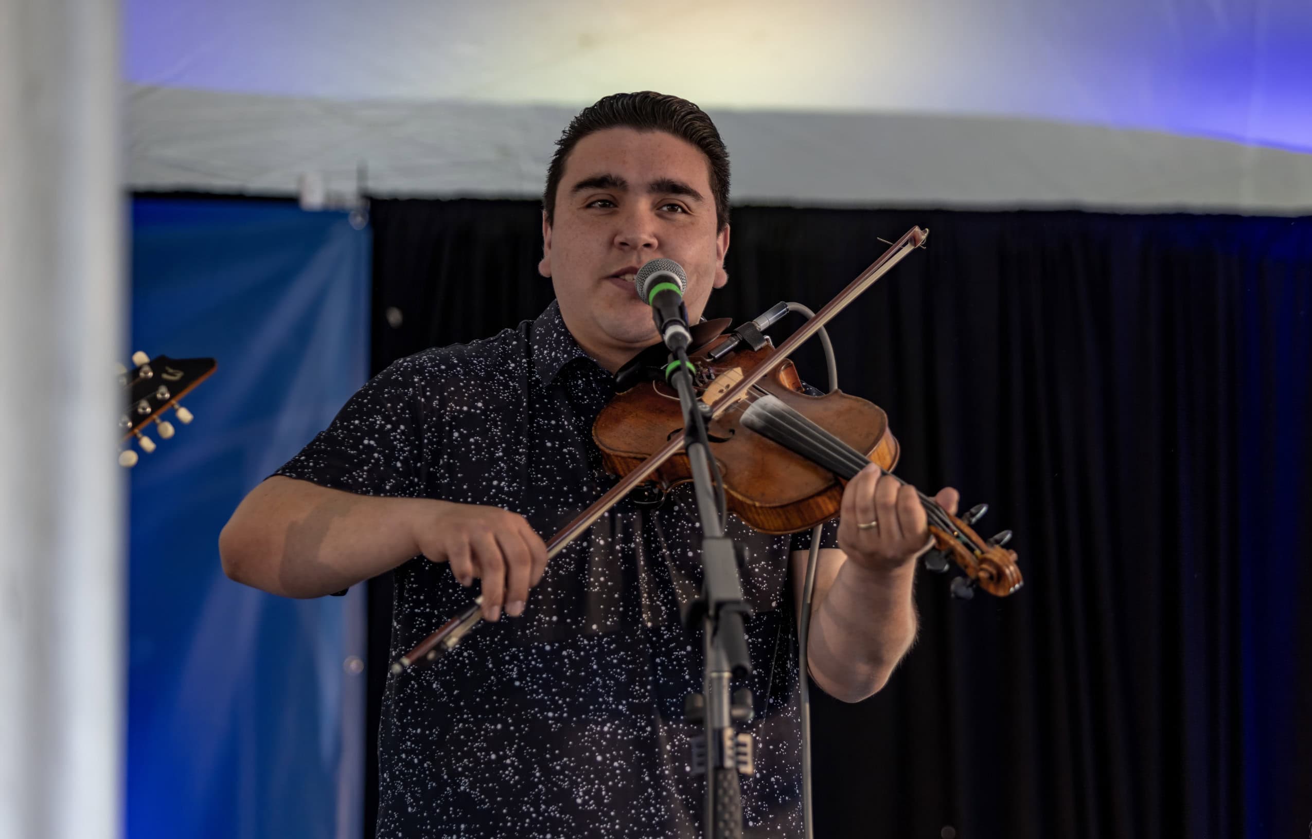A man plays violin and sings into a microphone.