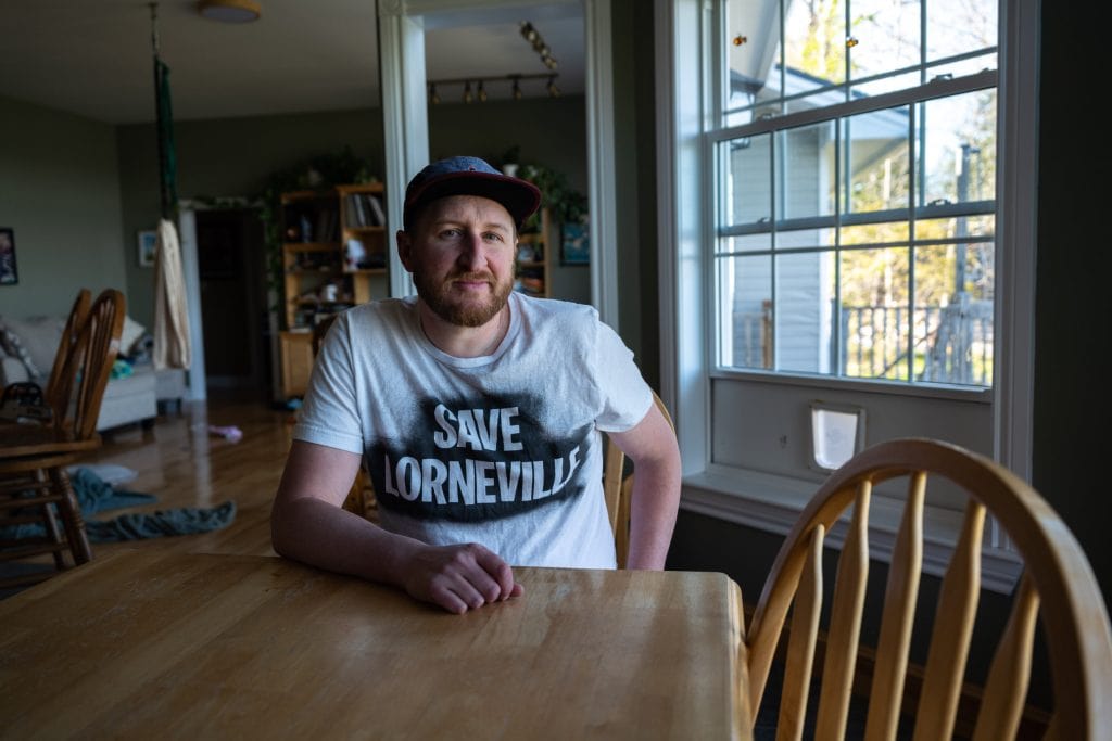 Adam Wilkins is seen at his home, wearing a t-shirt that says, "Save Lorneville."