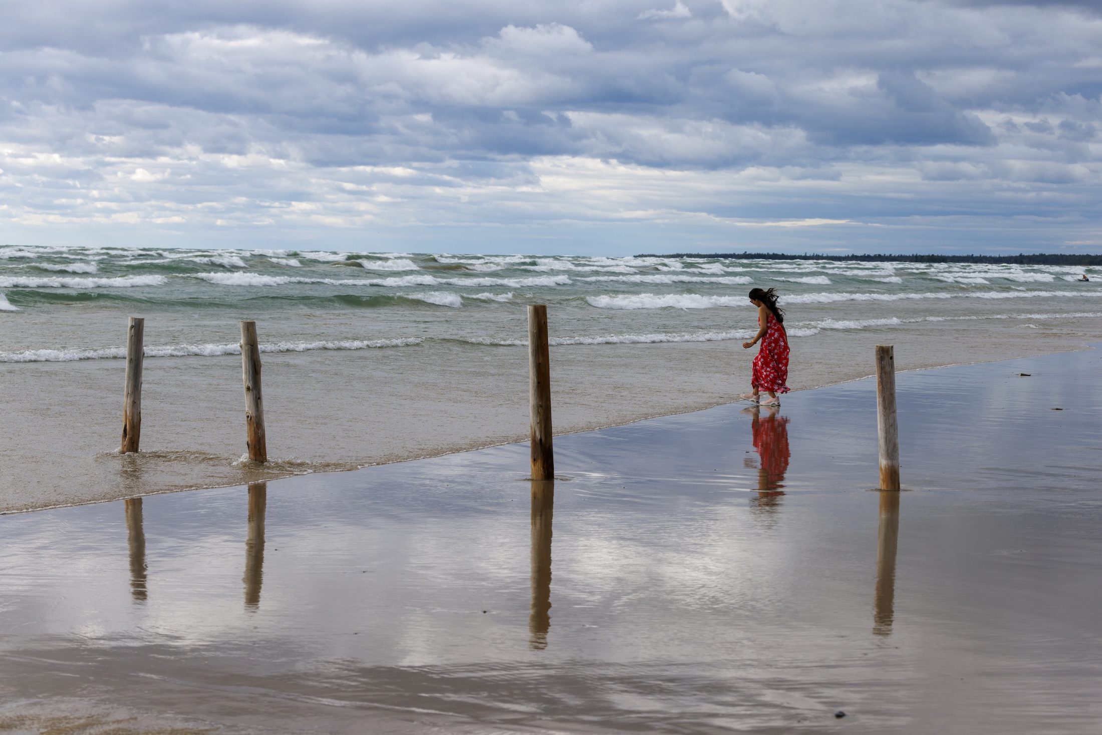 A person wearing a red dress walks along a beach while waves roll in.
