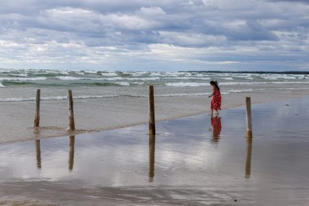 A person wearing a red dress walks along a beach while waves roll in.