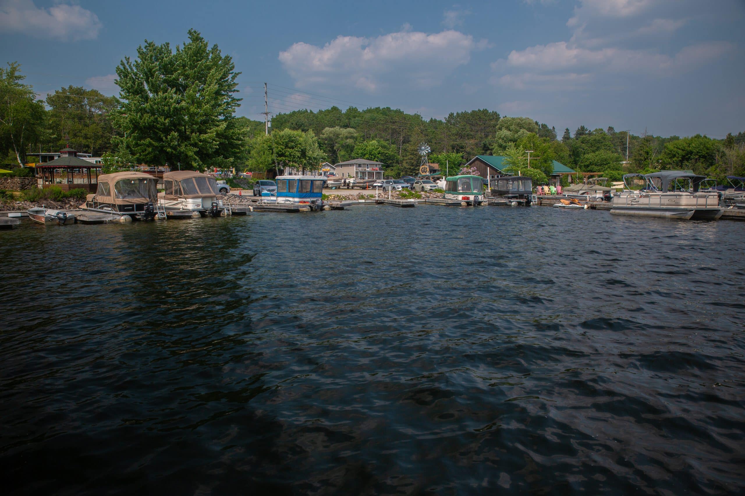 Trout Lake in North Bay, Ont is lined with boats and trees. The sky is blue with white clouds.