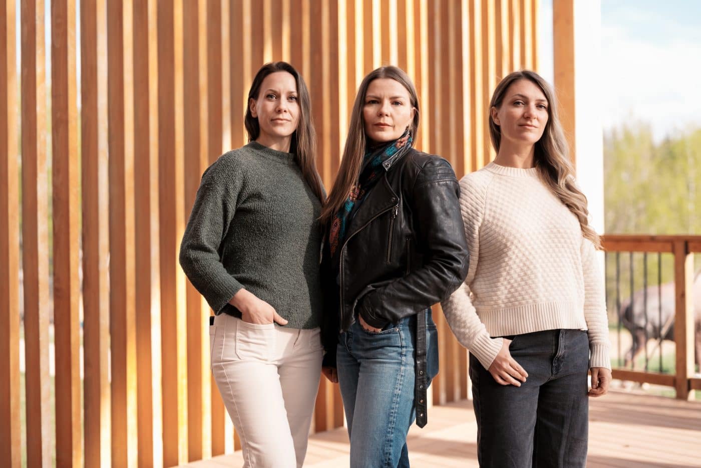 Caroll Linnitt, Amber Bracken and Emma Gilchrist stand side-by-side in front of a wood-clad building