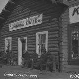A black-and-white photo of a building with a sign reading "Klondike Hotel" and men sitting on a bench in front of it.
