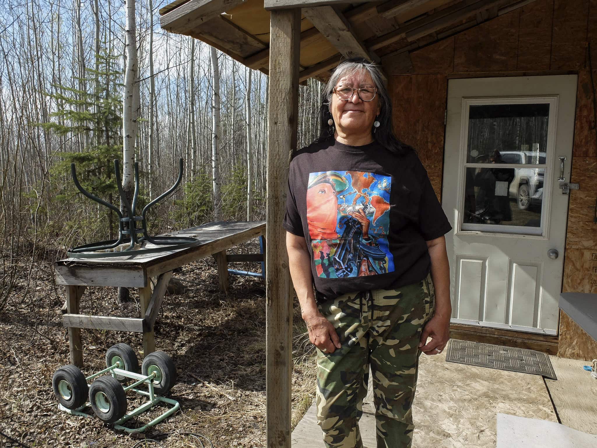 A woman leanign against the column of a wood cabin with forest behind it.