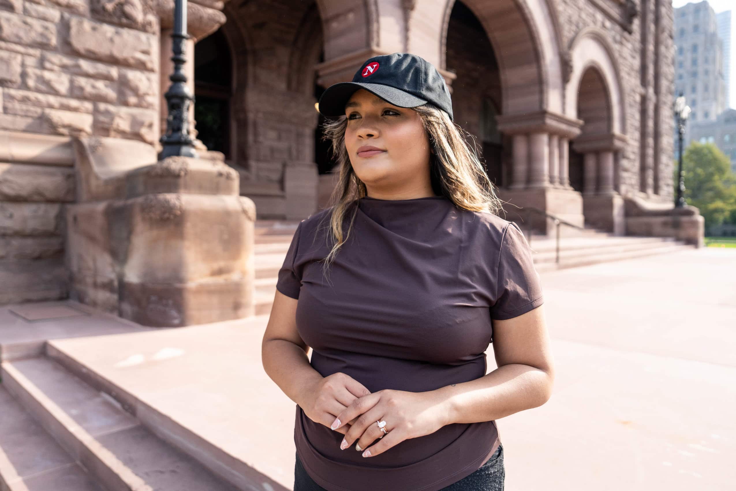 Reporter Rajpreet Sahota stands outside of Queen's Park in Toronto, wearing a baseball cap with The Narwhal's logo on it.