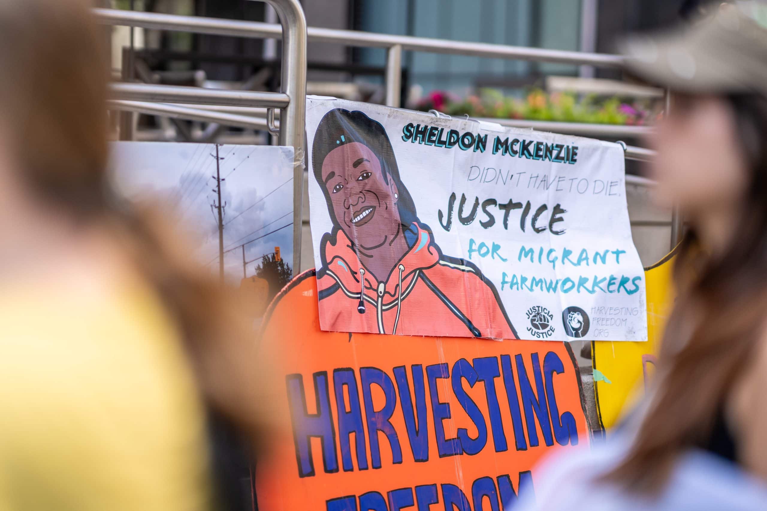 A sign shows a man with the writing "Sheldon McKenzie didn't have to die justice for migrant farmworkers"