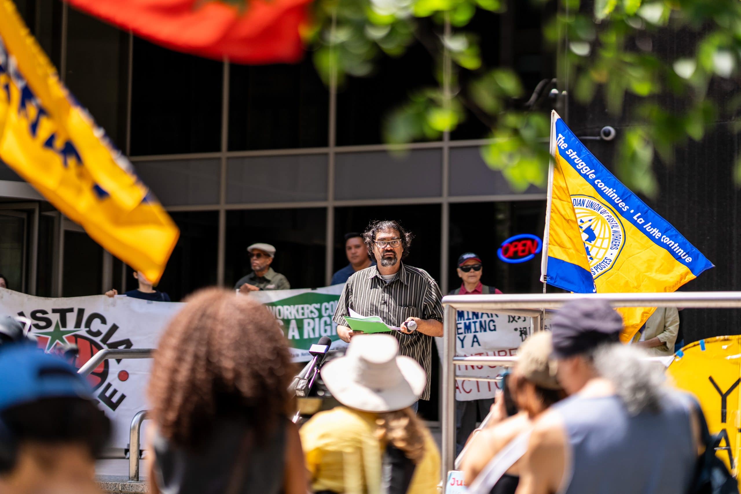 A man stands on the stairs in front of a group of people, there are people behind him holding signs