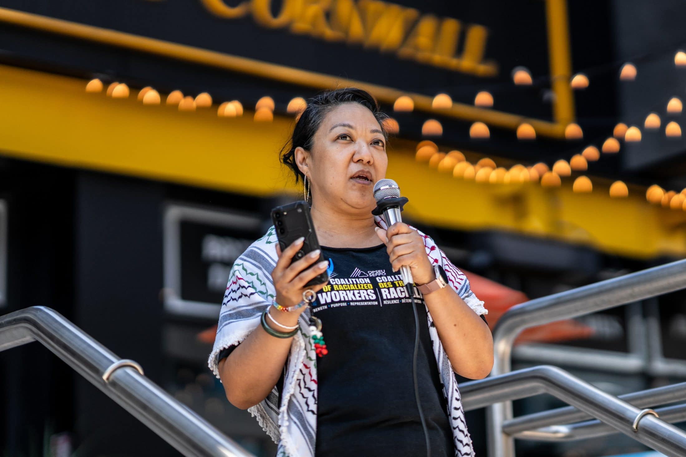 A woman holding a phone, speaks in to a microphone outside in Toronto