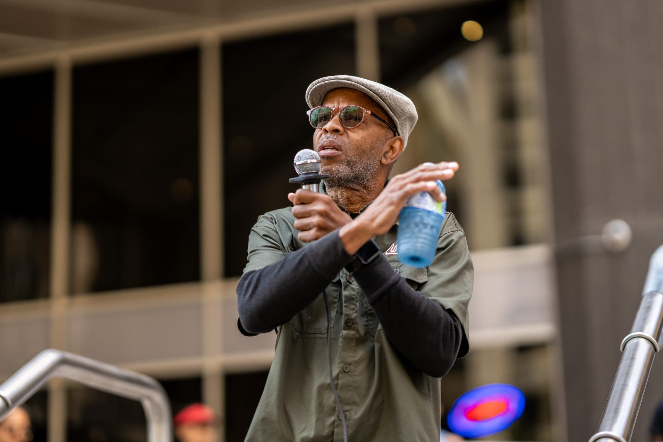 A man wearing a hat and sunglasses speaks into a microphone