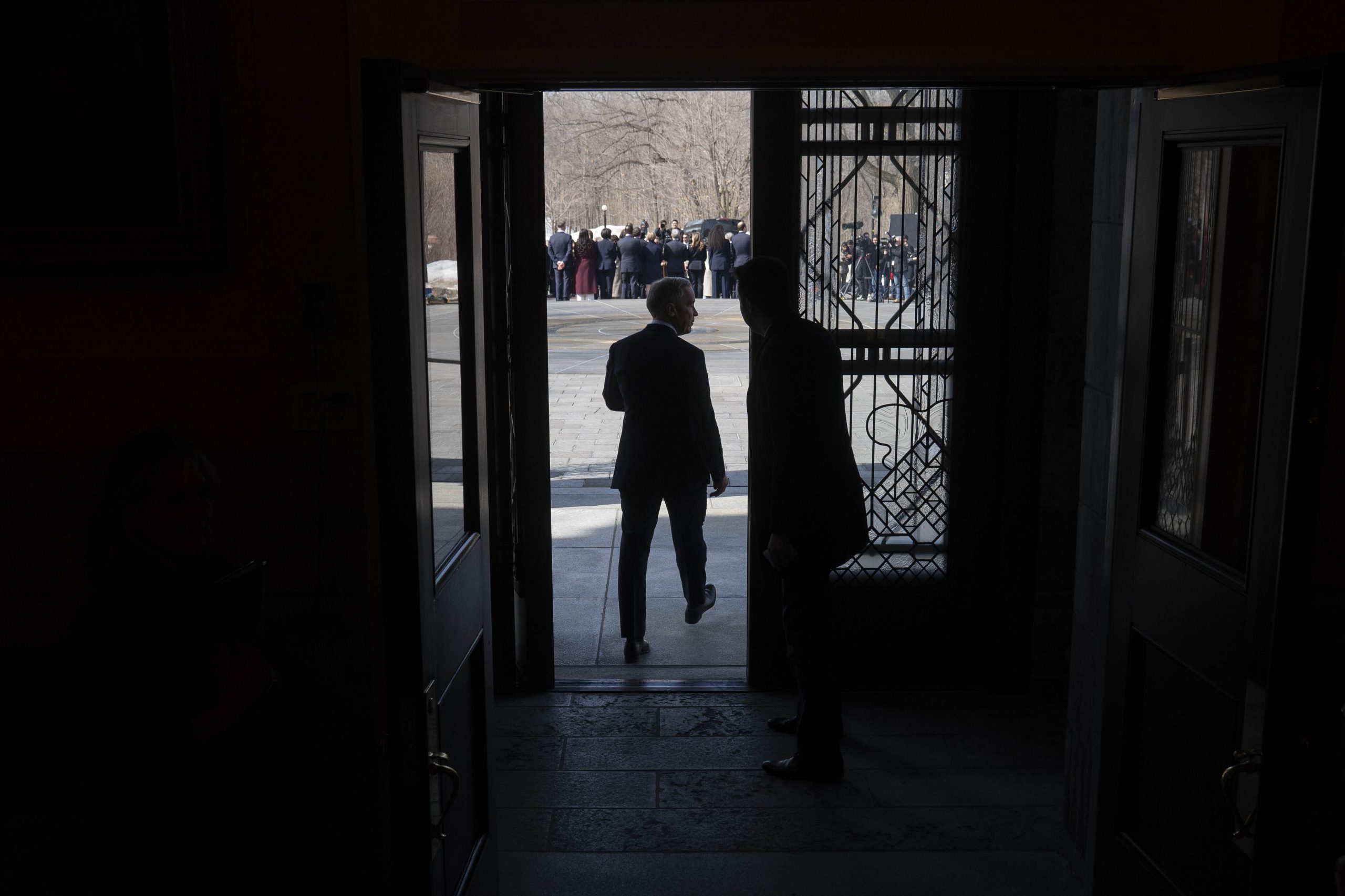 Prime Minister Mark Carney shadowed by sunlight outdoors, walks through a door