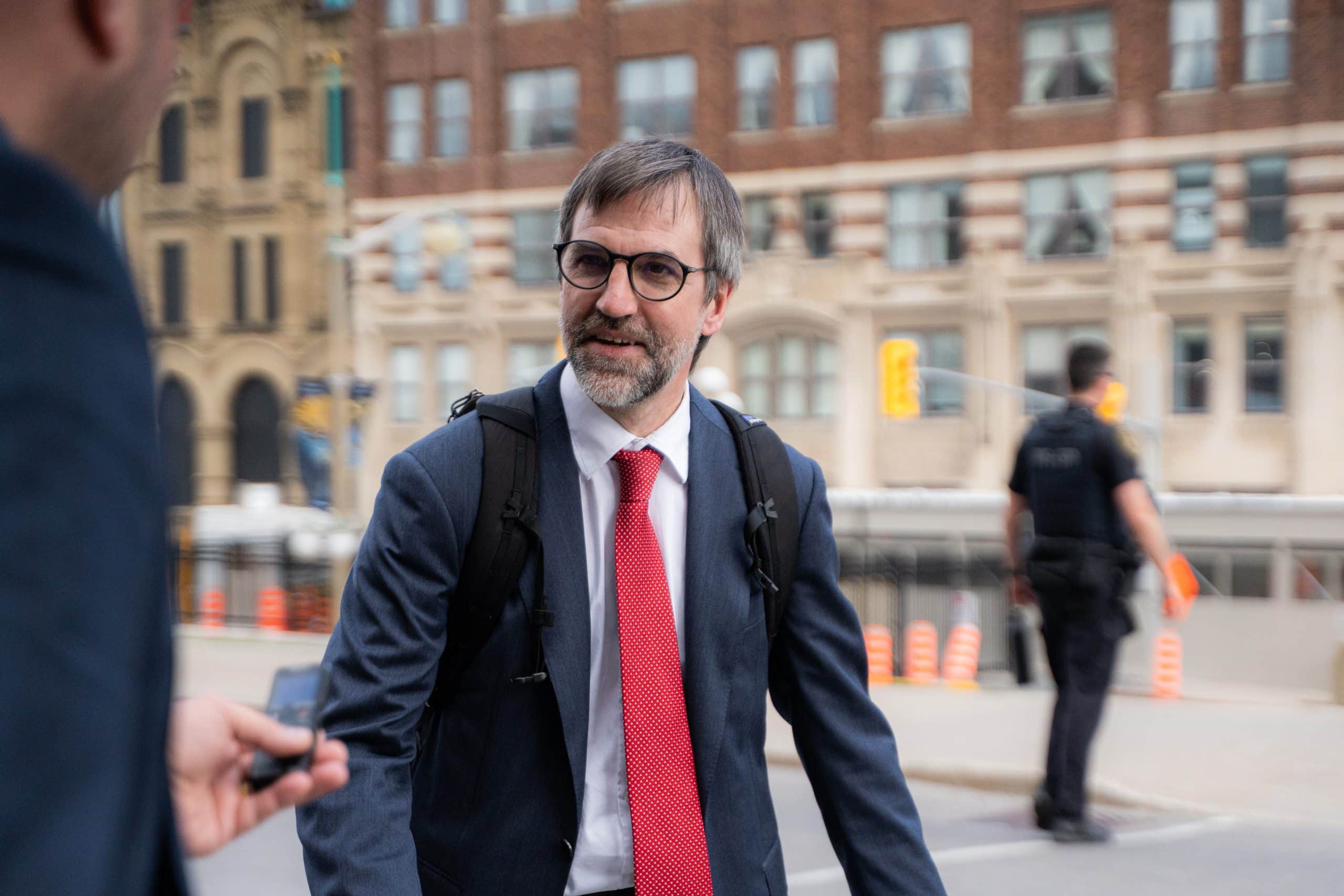Man in a suit smiles and speaks to a reporter in front of an office building.