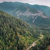 An aerial view of a mountain landscape that is mostly forested, except for areas that have been logged.
