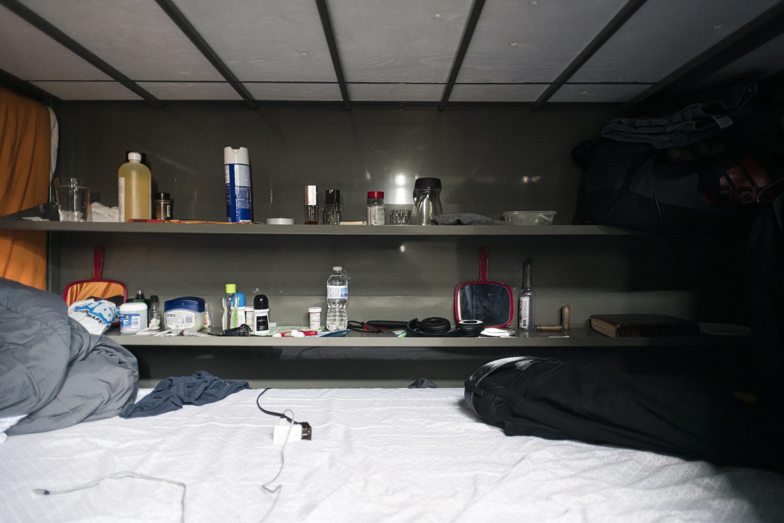 Personal items sit on two shelves behind a small mattress