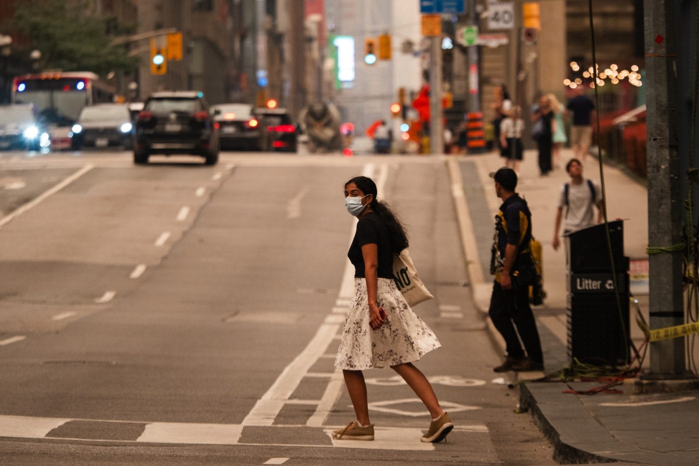 A person wearing a mask walks across a street in Toronto, as wildfire smoke blankets the city in July 2026.