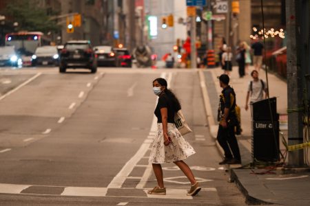 A person wearing a mask walks across a street in Toronto, as wildfire smoke blankets the city in July 2026.