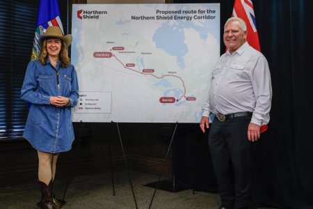 Danielle Smith and Doug Ford smile in front of a map displaying a proposed pipeline route from Alberta to Ontario