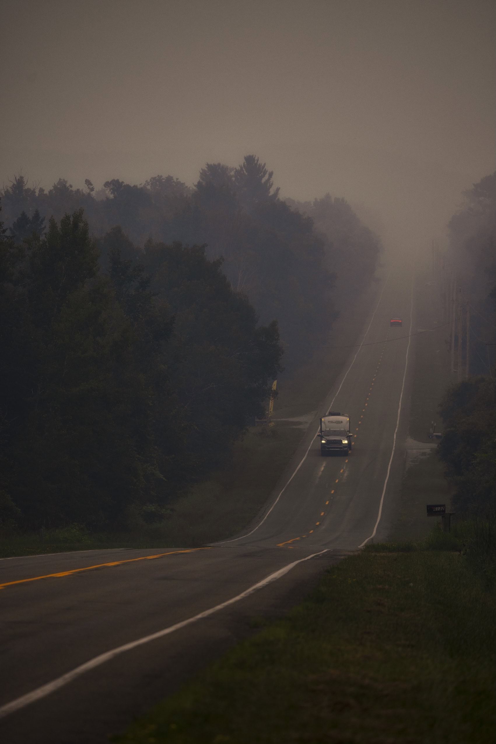 Vehicles drive down a two-lane road amid dense smoke from wildfires.